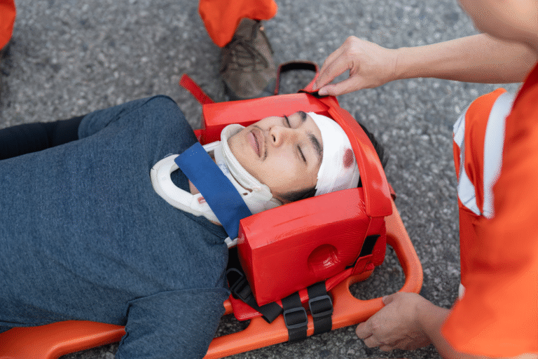 Paramedics stabilizing an injured person with a head wound and neck collar on a spine board during first aid treatment.