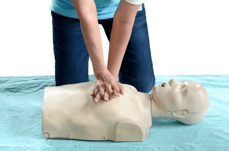 Person performing chest compressions on a CPR training manikin during a first aid practice session.